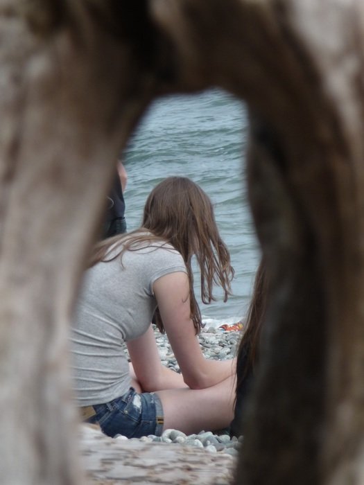 teenager sitting on a beach behind a rock