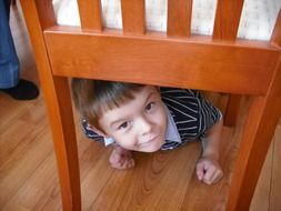 little boy hiding under a chair