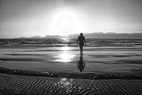 black and white photo of a child on the beach under the sun