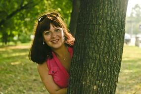 A girl looks out from behind a tree in the park
