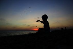 silhouette of a child throwing stones at sunset