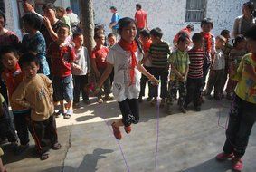 asian girl jumps with rope in circle of kids outdoor