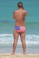 man stands on the beach in swimming trunks with a pattern of the usa flag