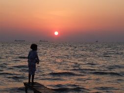 child on a pier near the ocean at sunset