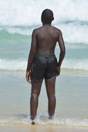 black man in swimming trunks stands in the water