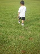 little boy in uniform walks on the lawn cut