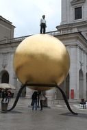 a man stands on a huge statue in the form of a golden ball