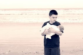 a boy with a baby in his arms by the sea