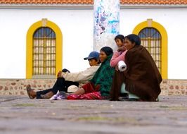 native people sitting on pavement at wall, bolivia, sucre
