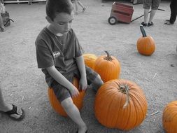 child boy sitting on pumpkin outdoor, monochrome