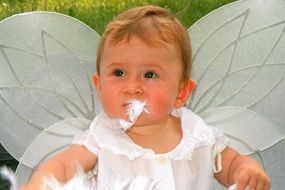 toddler in white costume with angel wings playing with feathers