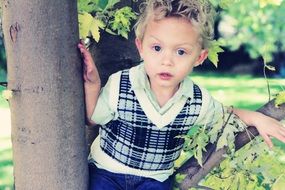 child in a plaid vest sits on a tree