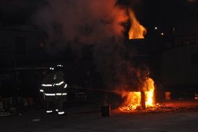 photo of two firefighters stand by a burning building in the dark