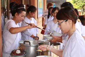 Women in white clothes give out food, Thailand