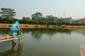man in a blue sweater is fishing on a quiet lake