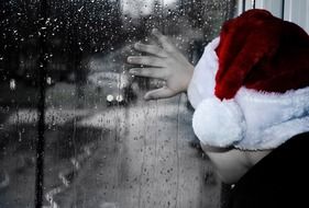 baby in Santa's hat looking out the rainy window