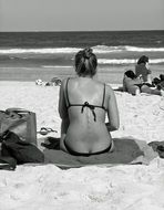 back view of young woman in bikini sitting on beach at sea