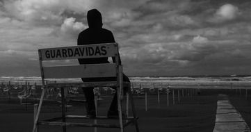 Black and white photo of the lonely man on a bench on the beach