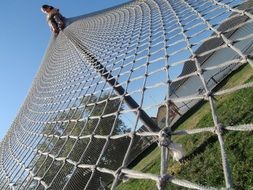 child girl sits at top of net on playground