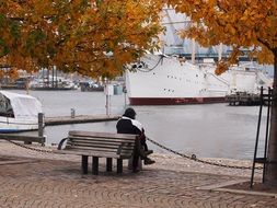 a lonely man sits on a bench by the river