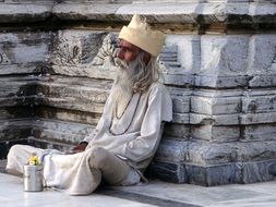 old bearded indian man sits at aged wall