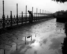 black and white photo of looking down man near the fence in rainy weather