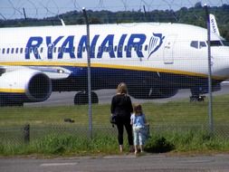 woman and girl looking at plane through fence