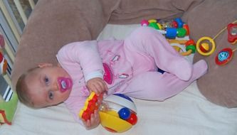 baby girl with pacifier in crib among toys