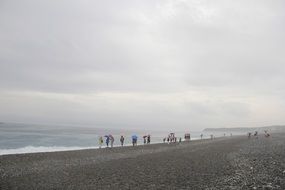 people looking at sea from beach in cloudy windy day