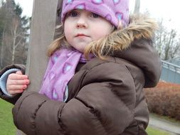 little girl in winter clothes near the post