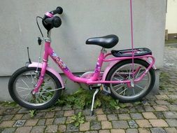 pink child bike near the wall on pavement