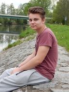 young boy sits in park on river bank at spring