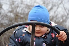 child in blue cap holding steering wheel outdoor