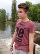 young man in a burgundy t-shirt by the river