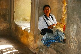 mature asian woman sits on window seal of temple, cambodia, ankor wat