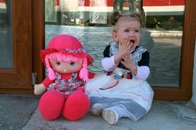 little girl sitting next to a doll