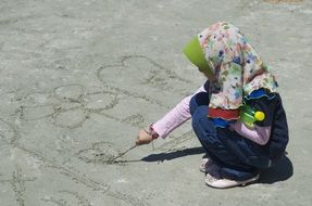 muslim girl draws on the sand with a stick