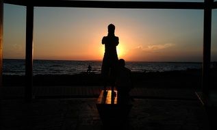 silhouettes of people looking at sunset above water
