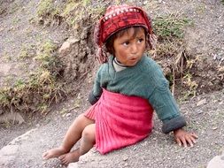 Peruvian little girl is sitting on a stone