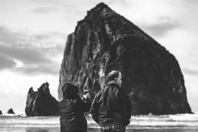 black and white photo of people on the beach near the cliff