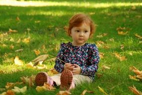baby girl sitting with yellow leaf in hand