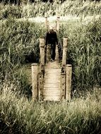 man on a wooden bridge among the grass