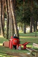 man is resting in a red plastic chair in the park