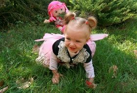 Little girl on grass on back with pink doll