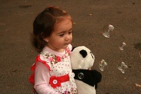 baby girl with teddy bear in hands on a background of soap bubbles