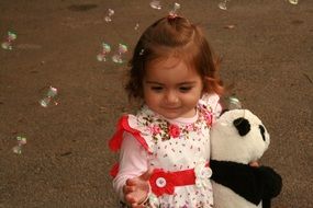 baby girl with teddy bear in hands playing with soap bubbles