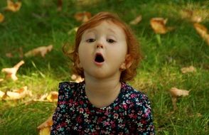 innocence in the face of a baby girl with russet hair on the background of autumn leaves