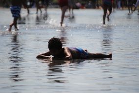 dark skin child girl lying down in water on street