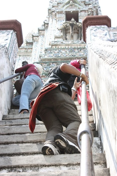 people climb the steep stairs of the temple