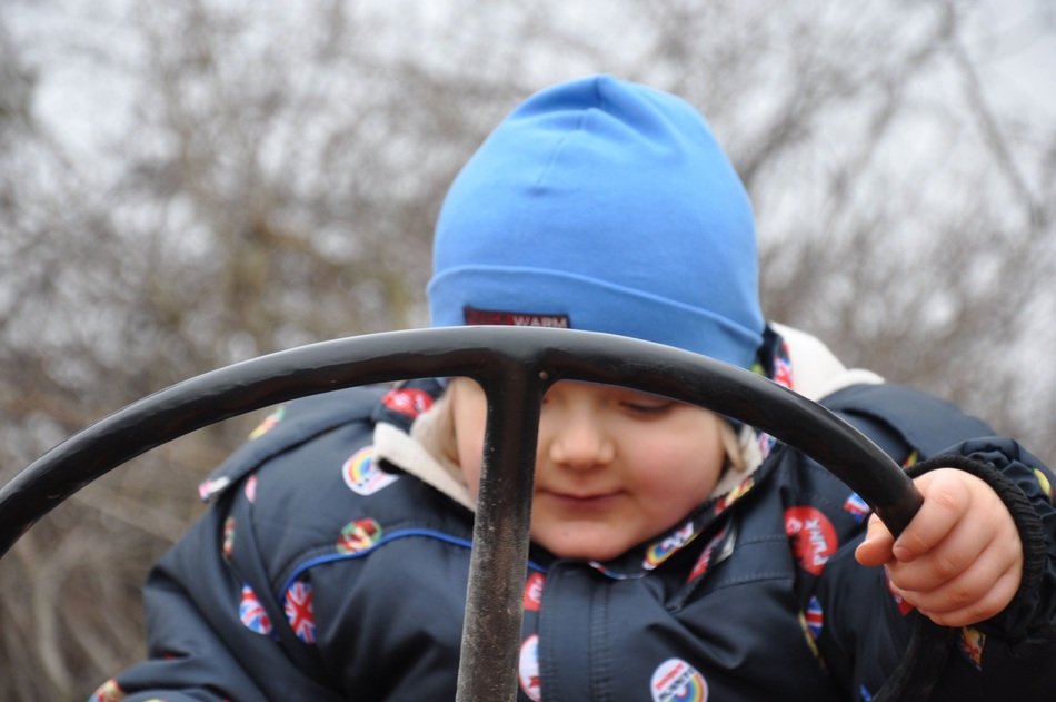 child in blue cap holding steering wheel outdoor